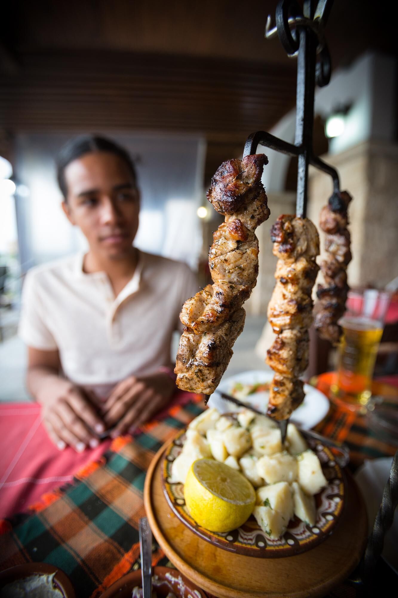 Una persona sentada a una mesa con carne ensartada y un plato de papas.