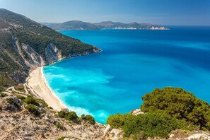 Un paisaje costero con playa, aguas azules cristalinas y terreno montañoso.