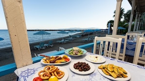 Ett bord med olika rätter, utsikt över stranden och blåa parasoller.