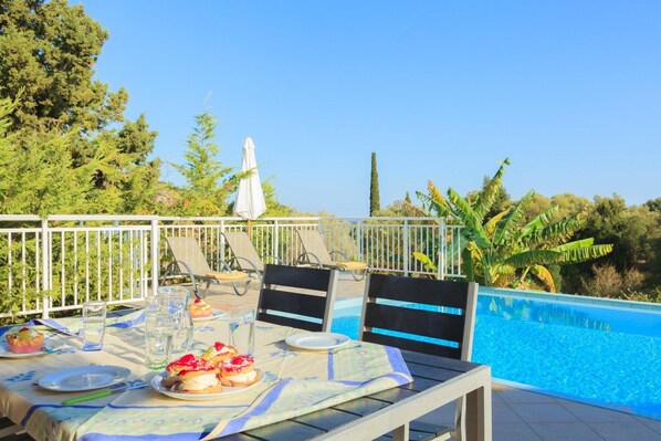 An outdoor dining area with a pool view, including tables, chairs, and a white fence.