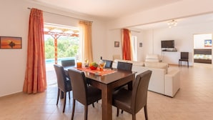 A dining area with a table set for four, a sofa, and a TV in the background. - Villa Peach Large Private Pool Walk to Beach Sea Views A C Wifi Car Not Required - 2181 (Kefalonia)