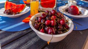 A dining table with a bowl of cherries, watermelon slices, and glasses of orange juice. - Villa Peach Large Private Pool Walk to Beach Sea Views A C Wifi Car Not Required - 2181 (Kefalonia)