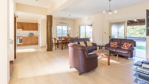 A spacious living area with a large brown leather sofa, a dining table, and a kitchen in the background. - Villa Clementina Large Private Pool Walk to Beach Sea Views A C Wifi Eco-friendly - 2183 (Ayia Marina Chrysochous)