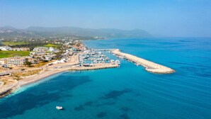 An aerial view of a coastal marina with boats docked, a pier extending into the sea, and a residential area with buildings and greenery in the background. - Villa Rose Large Private Pool Walk to Beach Sea Views A C Wifi - 2184 (Ayia Marina Chrysochous)