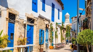 A narrow street with white buildings and blue shutters, a bell tower in the distance, and outdoor seating areas. - Villa Chrystalla Large Private Pool Walk to Beach Sea Views A C Wifi - 2186 (Neo Chorio)