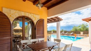 An outdoor patio with a wooden table and chairs, a pool, and a view of the mountains.