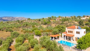 A modern villa with a swimming pool, surrounded by lush greenery and hills in the background.