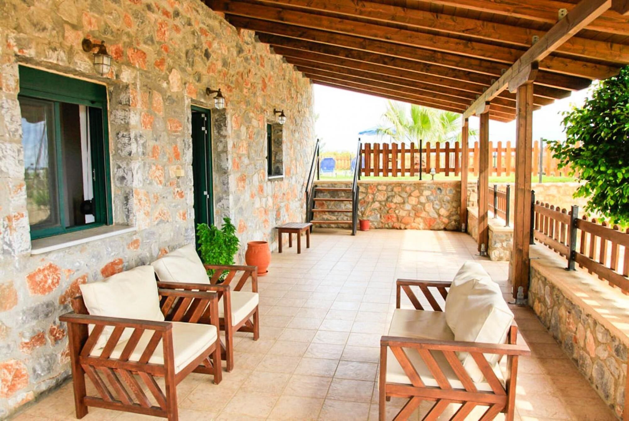 A covered outdoor seating area with stone walls, wooden furniture, and a view of the garden.