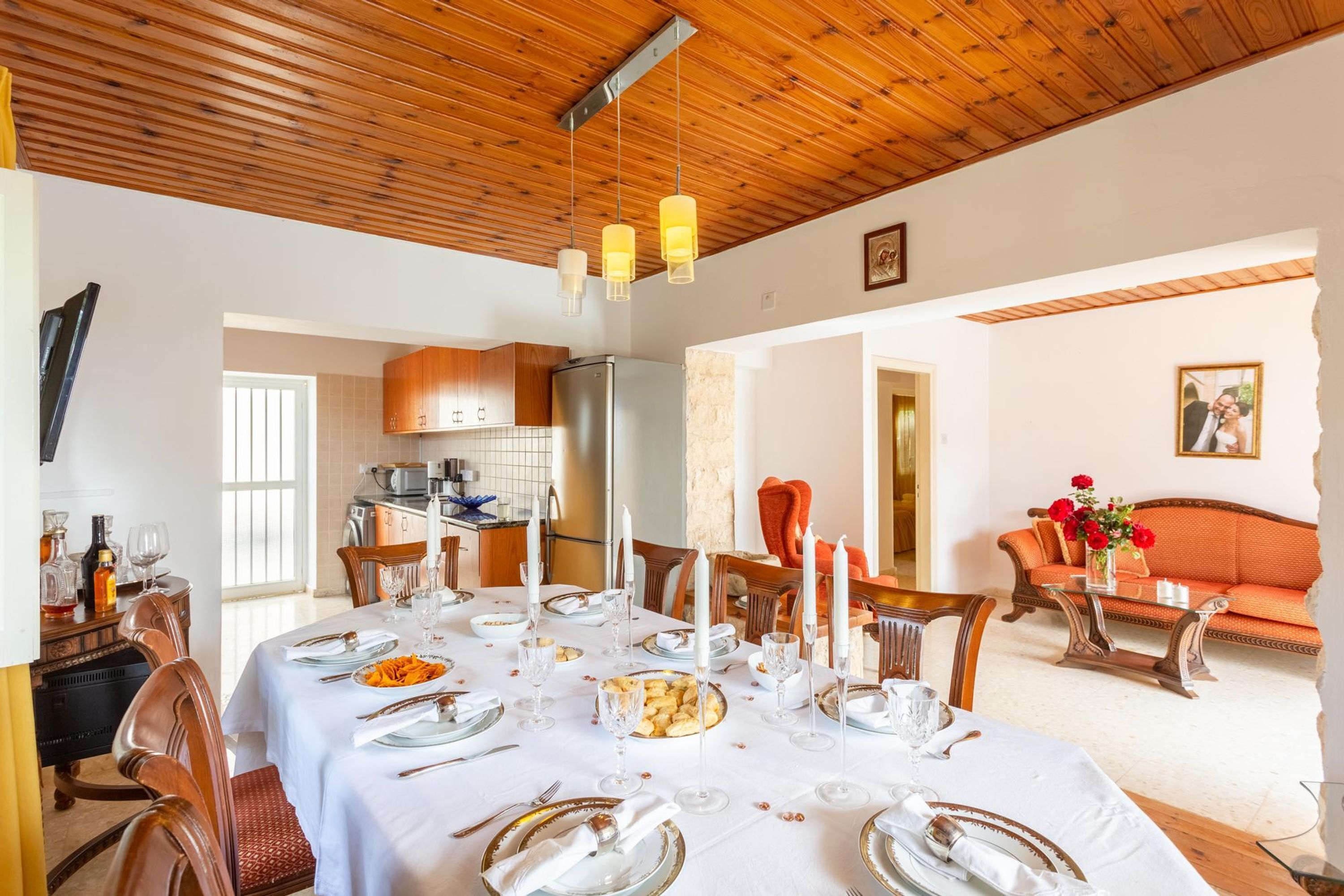 A dining area with a large table set for a meal, wooden ceiling, and a sofa in the background.