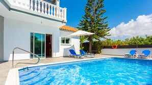Ein Swimmingpool mit klarem, blauem Wasser, umgeben von Liegestühlen und einem weißen Gebäude mit Balkon.