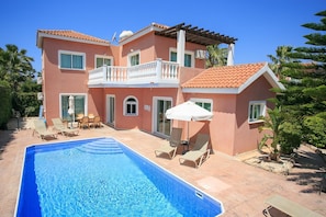 Une maison à deux étages avec une piscine, un espace salon extérieur et une terrasse couverte.