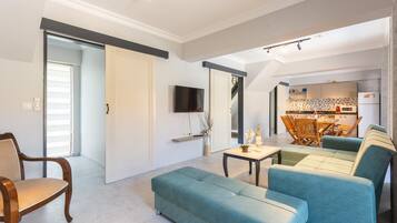 A modern living room with a sofa, a wooden chair, and a dining area with a table and chairs.