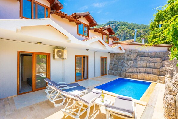 A modern villa with a swimming pool, outdoor seating, and a stone wall.