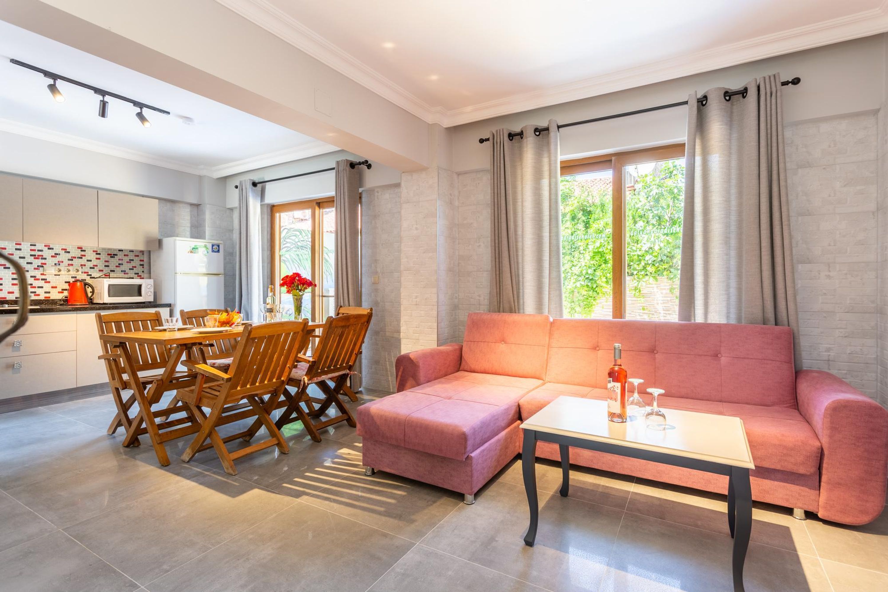 A modern living room with a pink sofa, a dining table with chairs, and a kitchen area with a microwave and cabinets.