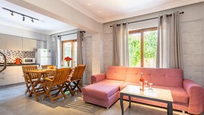 Een moderne woonkamer met een roze bank, een eettafel met stoelen en een keuken met een magnetron en kastjes.