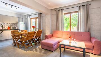 A modern living room with a pink sofa, a dining table with chairs, and a kitchen area with a microwave and cabinets.
