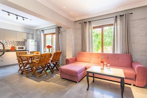 Ein modernes Wohnzimmer mit einem rosafarbenen Sofa, einem Esstisch mit Stühlen und einer Küchenzeile mit Mikrowelle und Schränken.