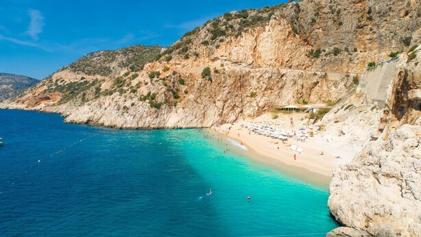 A coastal beach with clear turquoise waters, rocky cliffs, and a few beach umbrellas. - Villa Melek Paradise Private Pool A C Wifi Car Not Required Eco-friendly - 2235 (Ortaca)