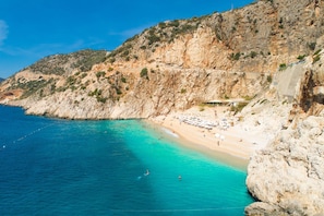 A coastal beach with rocky cliffs, a sandy shore, and a clear blue sea.