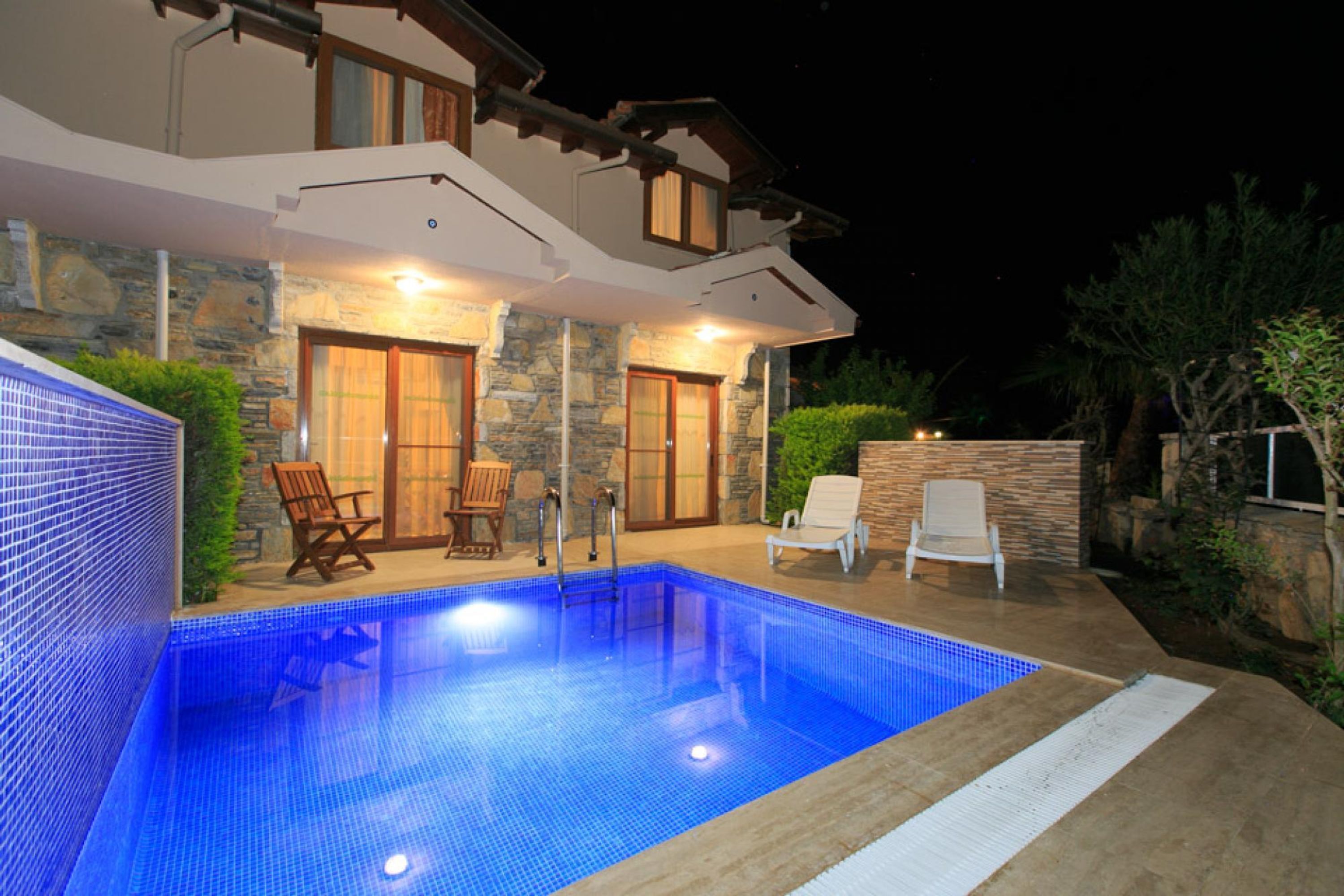 Ein Schwimmbecken mit Steinverkleidung und Liegestühlen aus Holz.