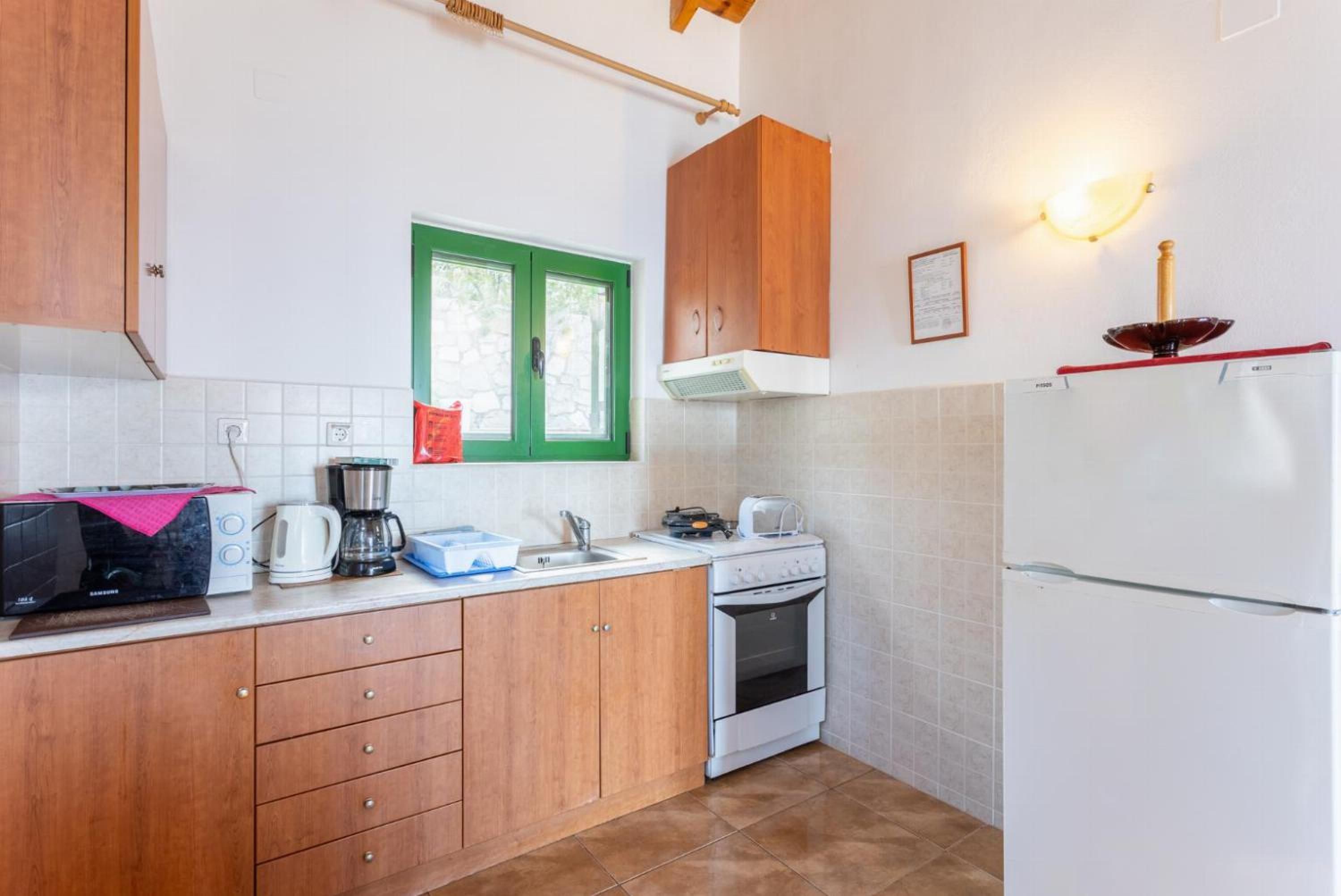 Una cocina compacta con armarios de madera, un refrigerador blanco, una estufa y una ventana con marco verde.