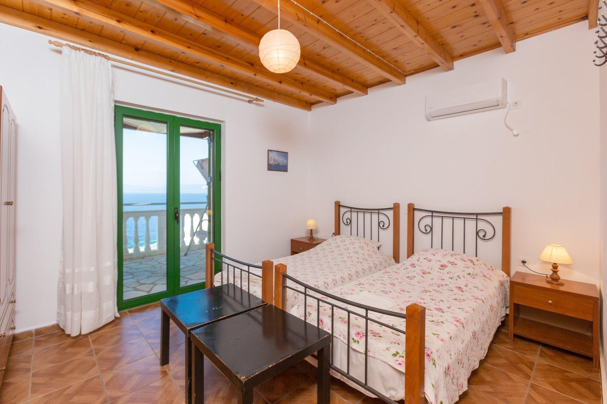 A bedroom with a bed, bedside tables, a small table, a view through a green door, and a ceiling fan.