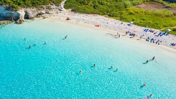 An aerial view of a beach with clear turquoise water, people swimming, and sun loungers along the shore. - Villa Anastasia Large Private Pool Walk to Beach Sea Views A C Wifi Car Not Required - 2248 (Paxos)