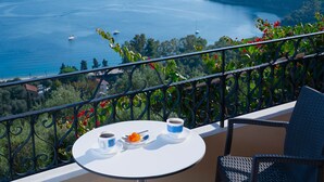 Un balcón con una mesa lista para dos personas, con vistas a la costa, barcos y vegetación.