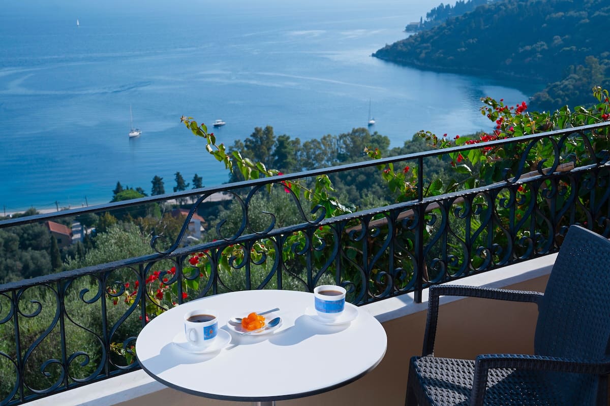 Un balcon avec une table dressée pour deux personnes, offrant une vue sur la côte, avec des bateaux et une végétation luxuriante.
