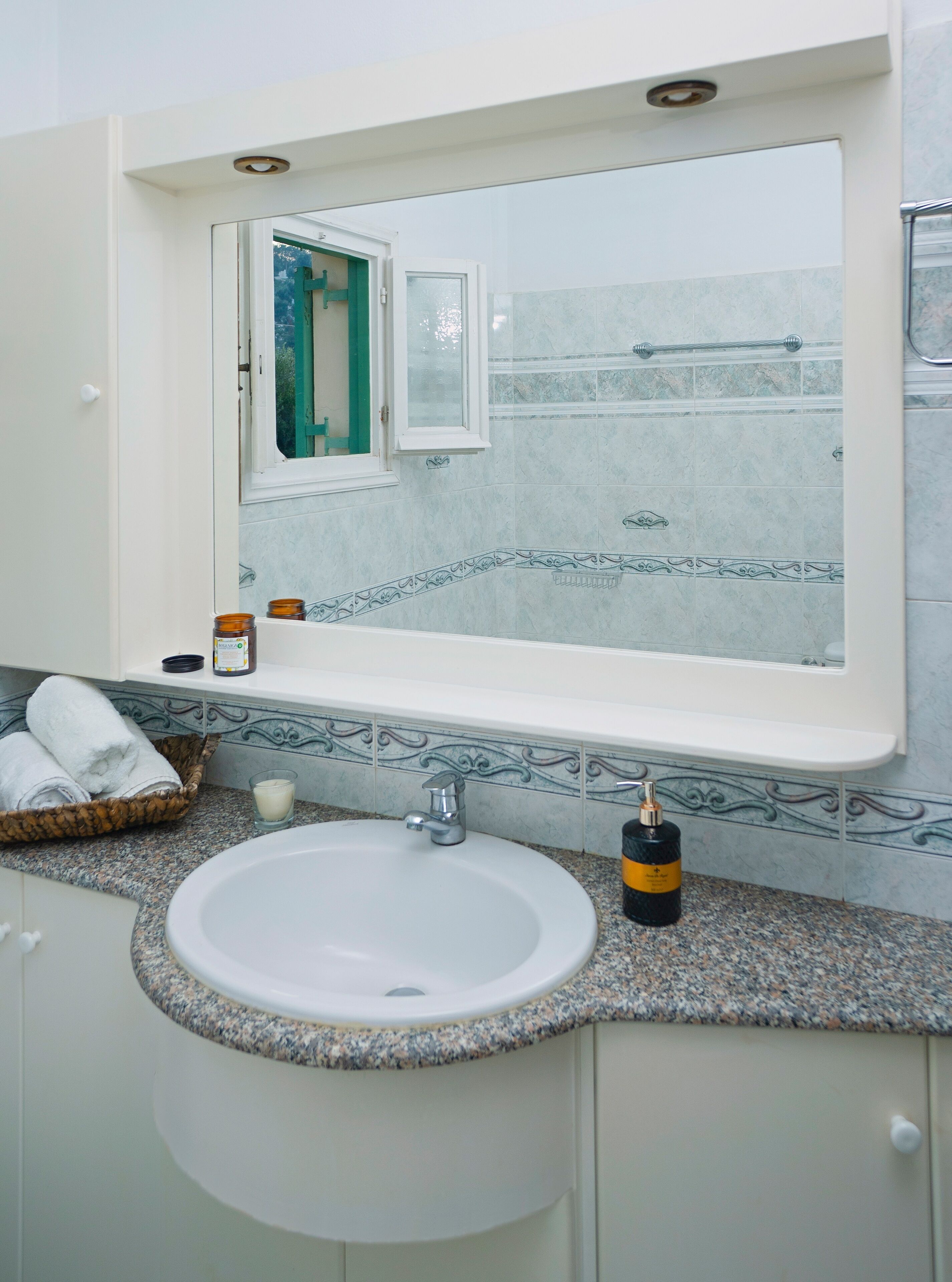 Un bagno con un lavandino bianco, uno specchio sopra e una finestra con cornice verde.