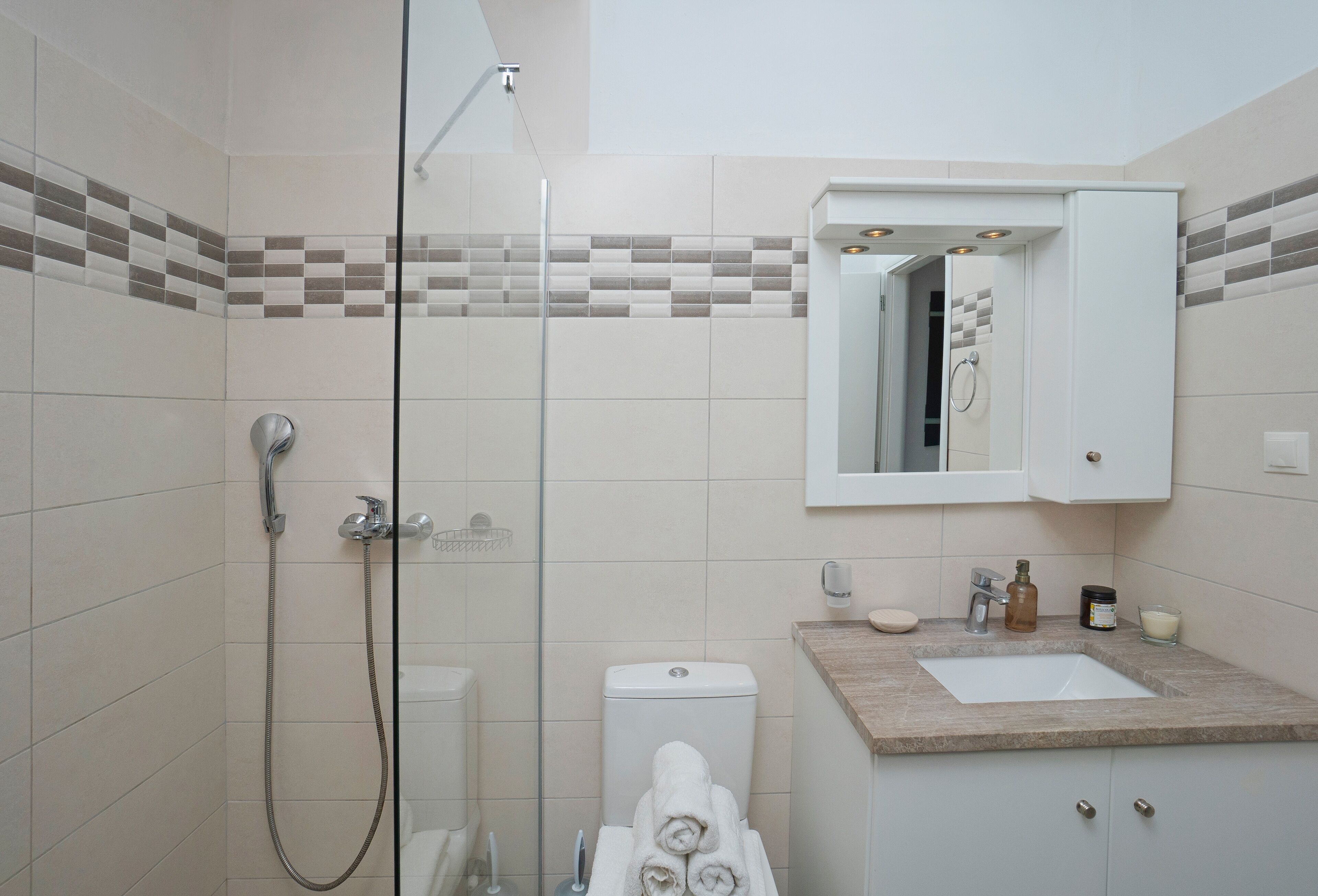 Un baño moderno con ducha envuelta en vidrio, inodoro, lavamanos con espejo y un perchero para toallas.