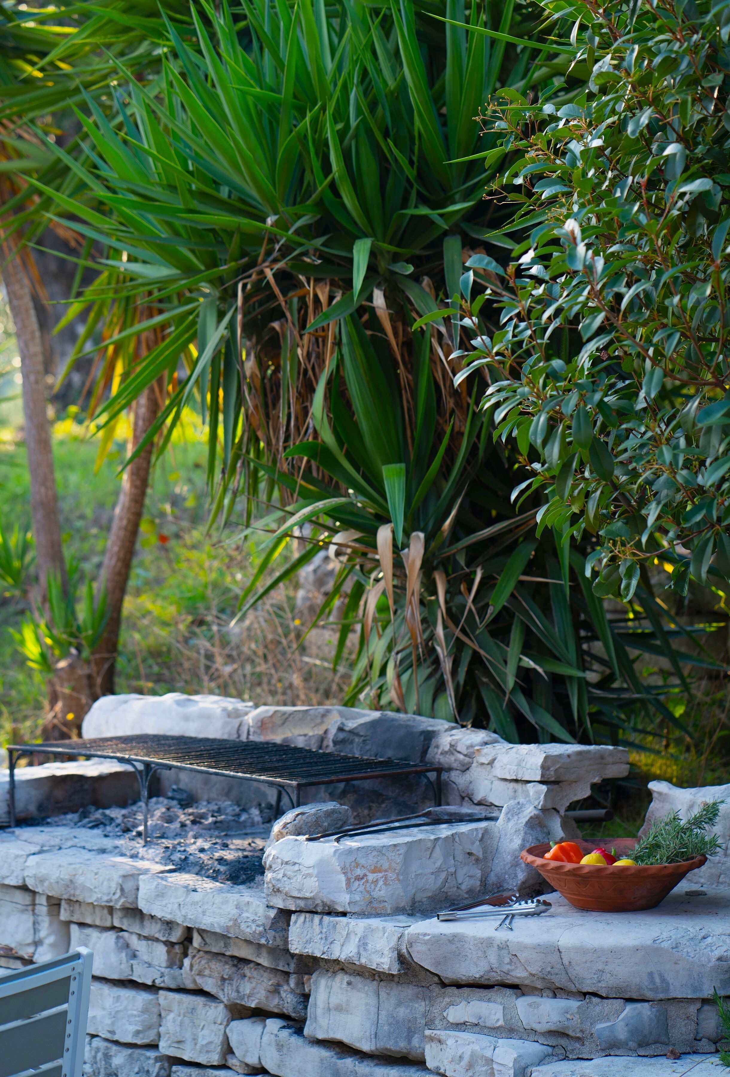 A stone barbecue grill with a bowl of fruit and utensils on a stone ledge.