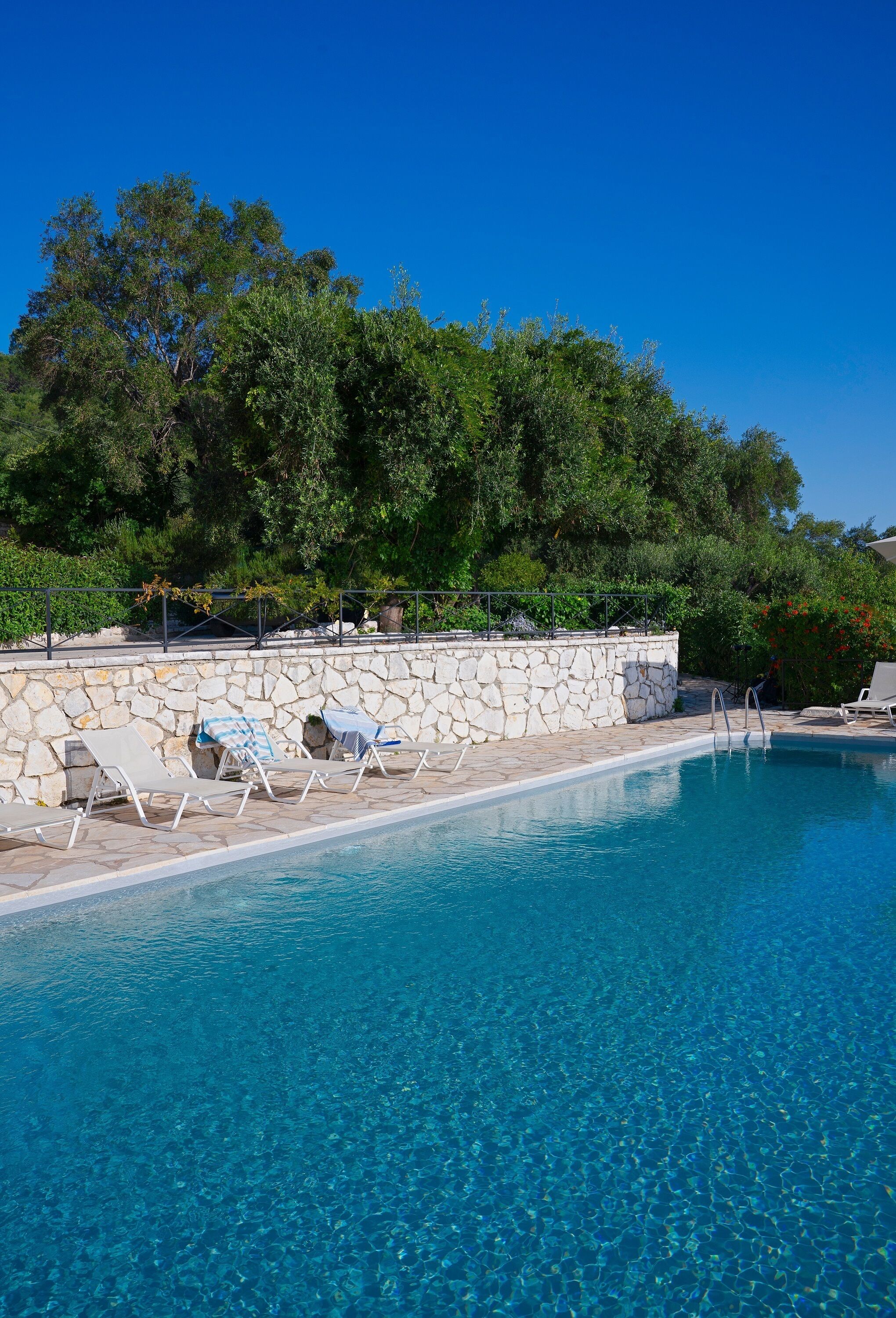 A clear blue pool with lounge chairs and a stone wall.