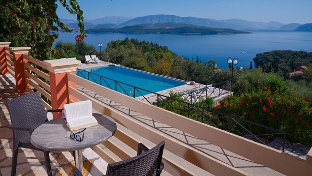 Una terraza con piscina, asientos al aire libre y vistas a un lago y montañas.