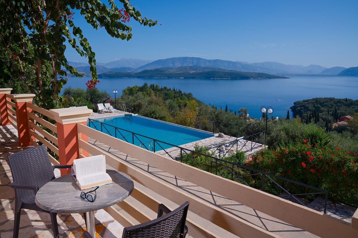 Une terrasse avec piscine, des sièges d’extérieur et une vue sur un lac et des montagnes.