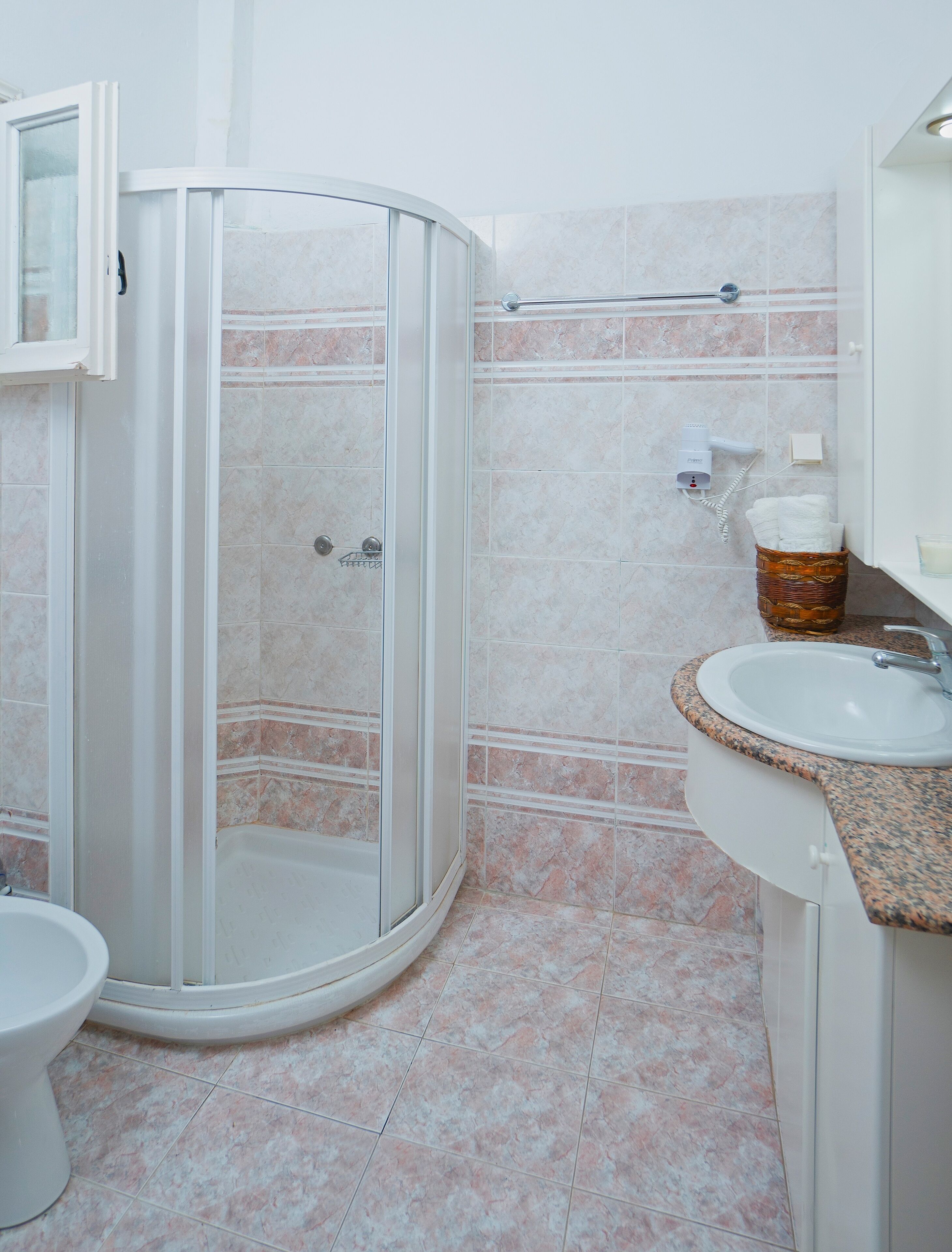 A bathroom with a glass-enclosed shower, a sink with a granite countertop, and a toilet.