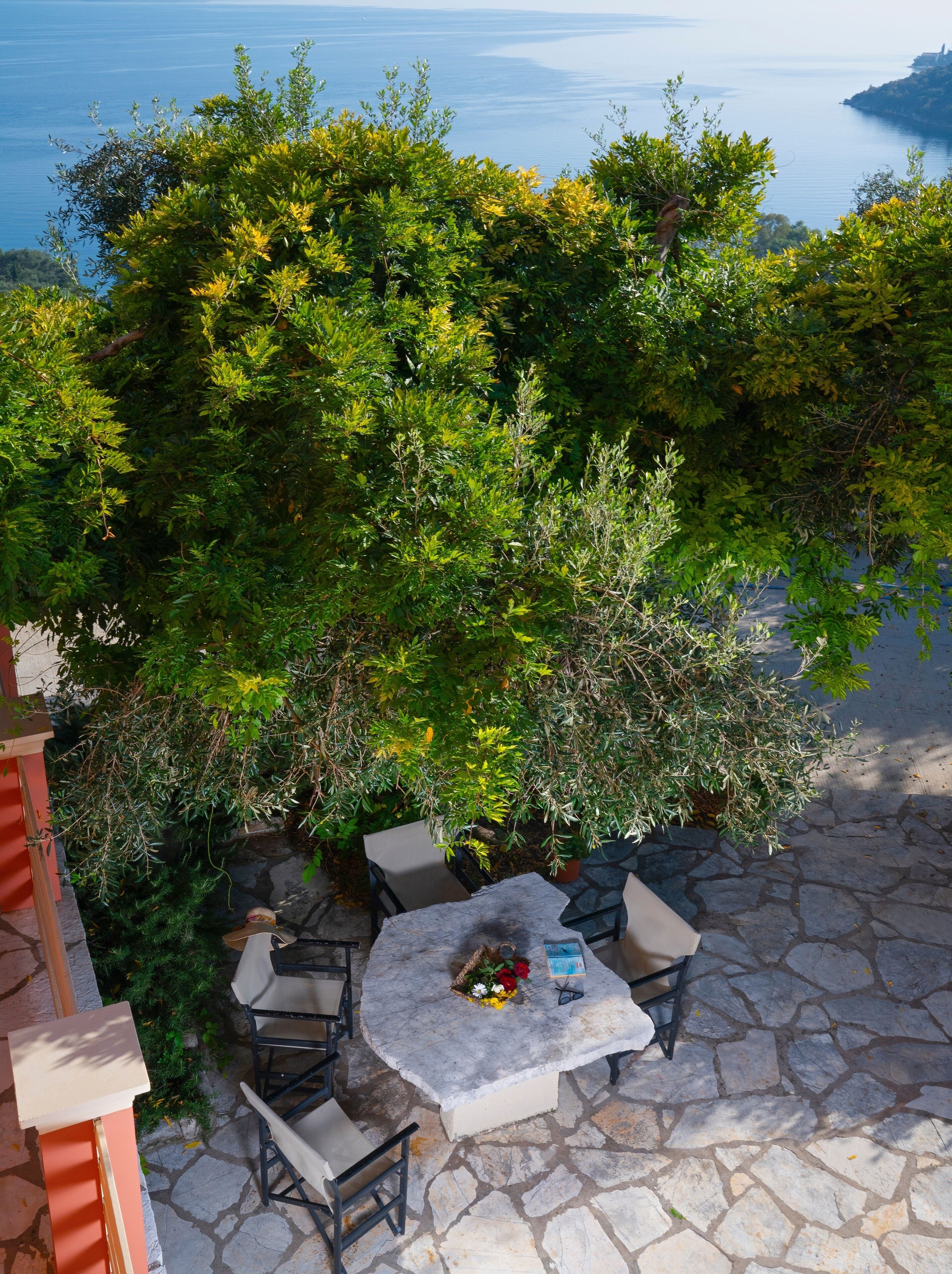 An outdoor seating area with a stone table and chairs, surrounded by lush greenery and overlooking a body of water.