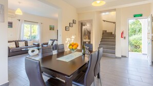 A modern living room with a sofa, dining table, and chairs. There is a staircase leading to an upper floor.