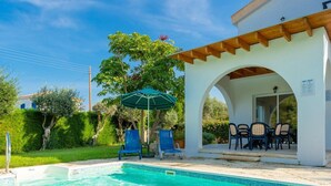 A clear swimming pool with blue water, surrounded by a white building with a covered patio area.