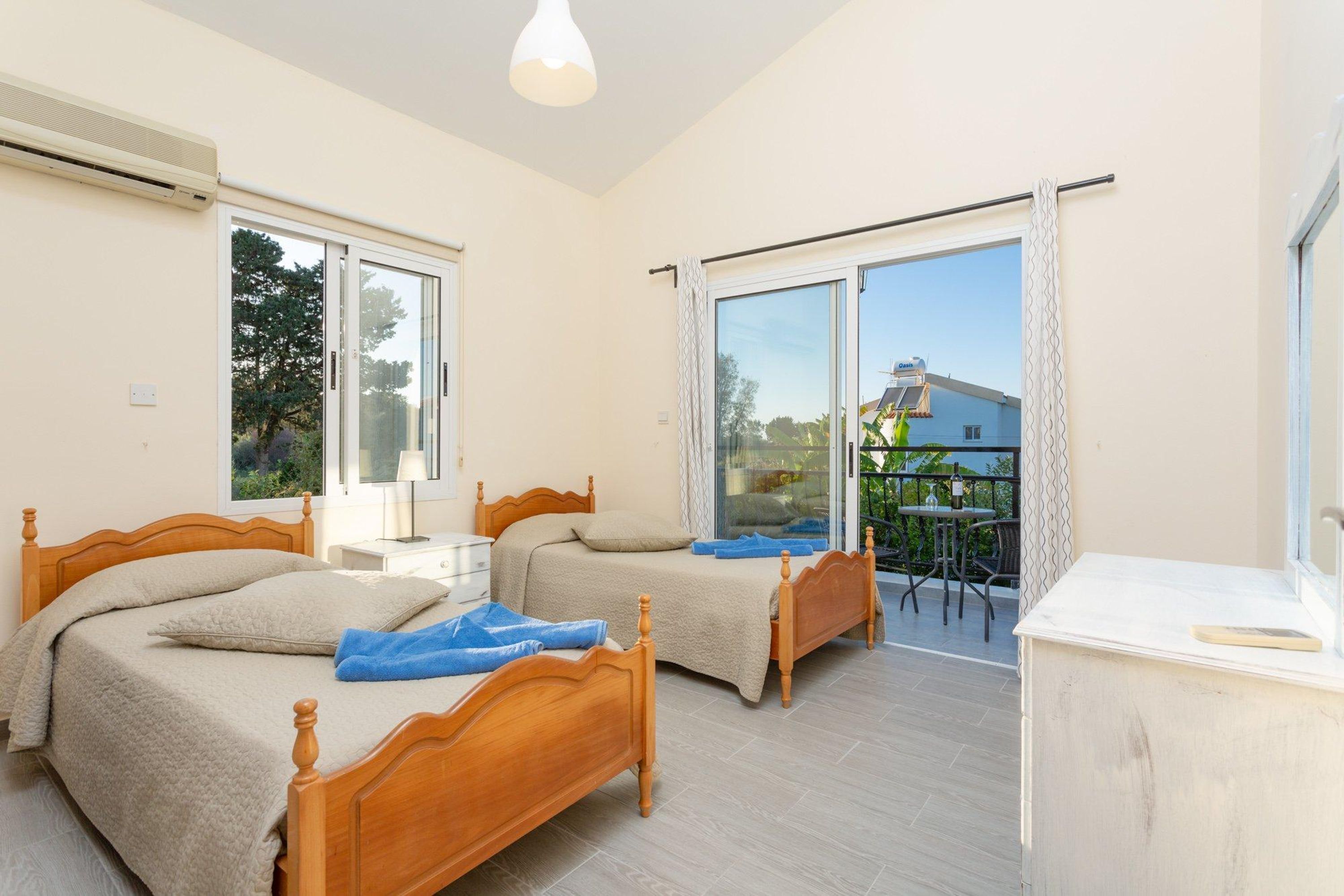 A bedroom with two wooden beds, a balcony with a table and chairs, and a large window.