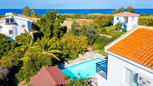 A residential area with a swimming pool, white buildings, and a view of the sea.