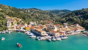 Une ville côtière dotée d’un port de plaisance rempli de bateaux, entourée de maisons à étages et de collines.