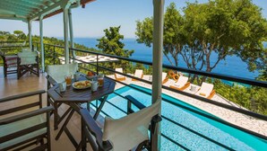Un espace aménagé au bord de la piscine, avec vue sur la mer, des sièges d’extérieur et une table où sont servis les articles du petit-déjeuner.
