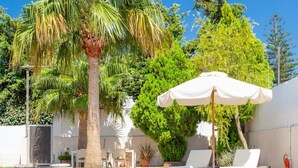 Une piscine entourée de palmiers et de verdure, avec des chaises longues et des parasols.