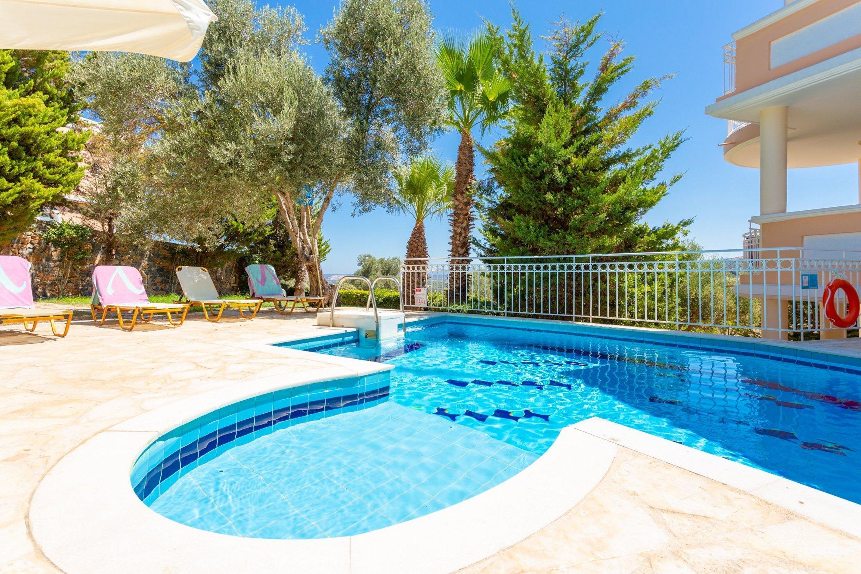 A swimming pool with a curved edge, surrounded by lounge chairs and palm trees.