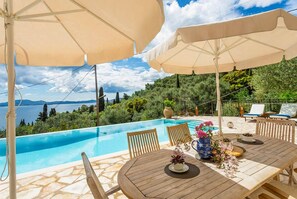 Un espace extérieur avec une piscine, une table et des chaises, entouré de parasols et de plantes en pot.