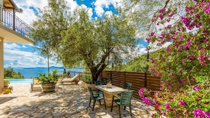 Un patio al aire libre con suelo de piedra, una mesa, sillas y vista al mar.