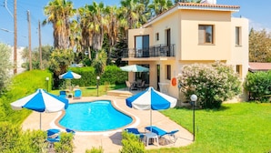 Un edificio de dos pisos con piscina, mobiliario exterior y palmeras.
