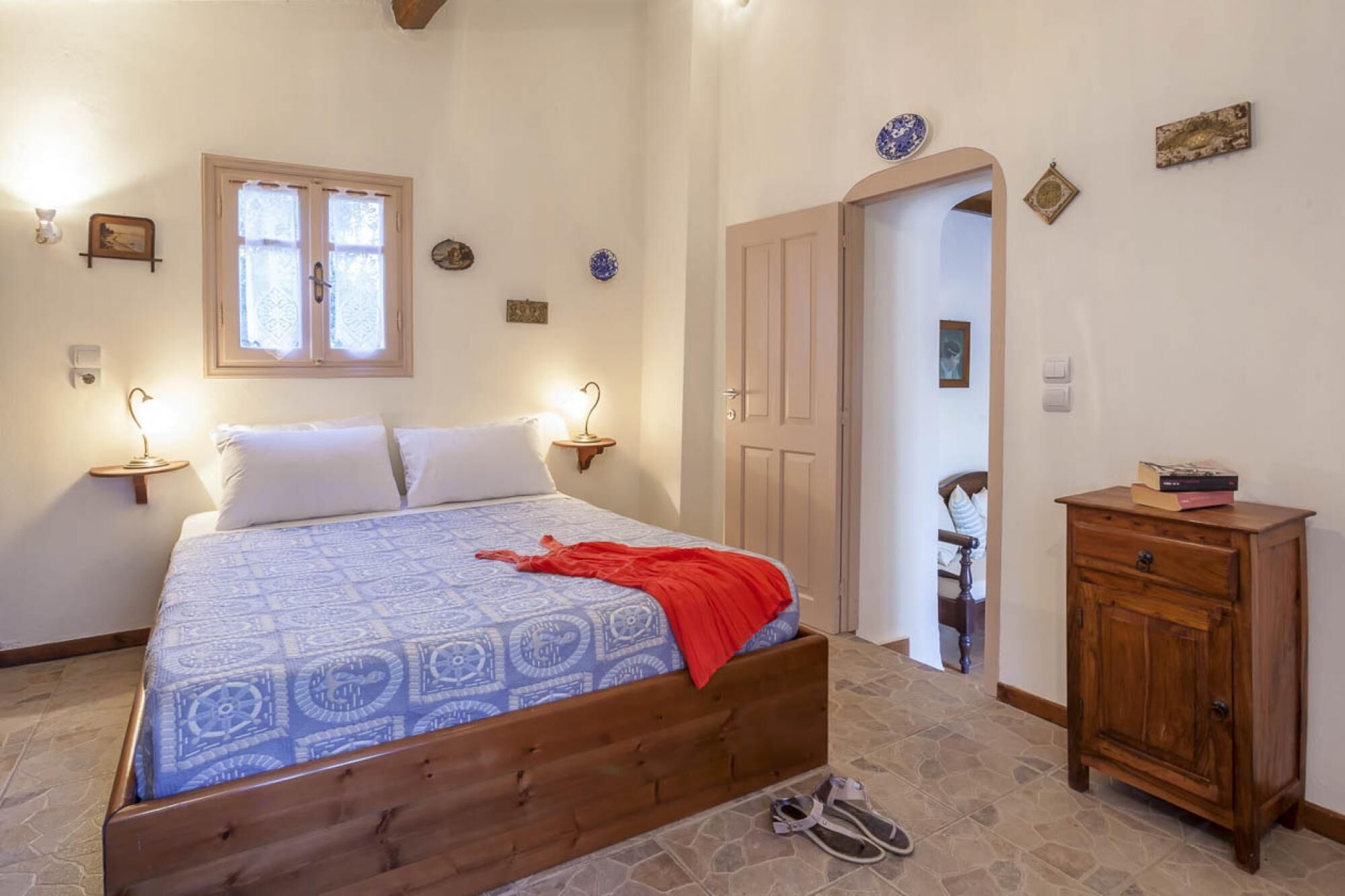 Quarto com cama de madeira, mesa de cabeceira, penteadeira e janela com cortinas estampadas.