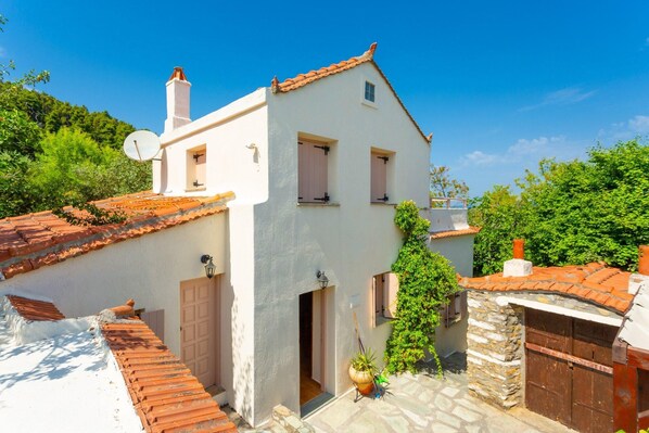 Un bâtiment blanc avec un toit recouvert de tuiles, une antenne parabolique et un mur en pierre.